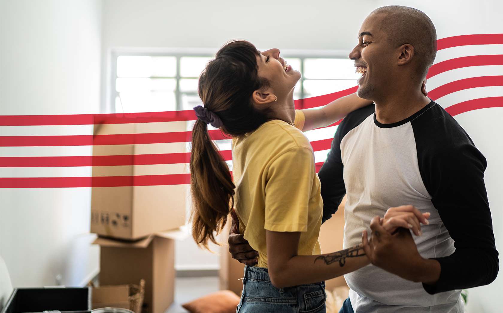 Smiling couple dancing closely in a sunlit room with moving boxes in the background.